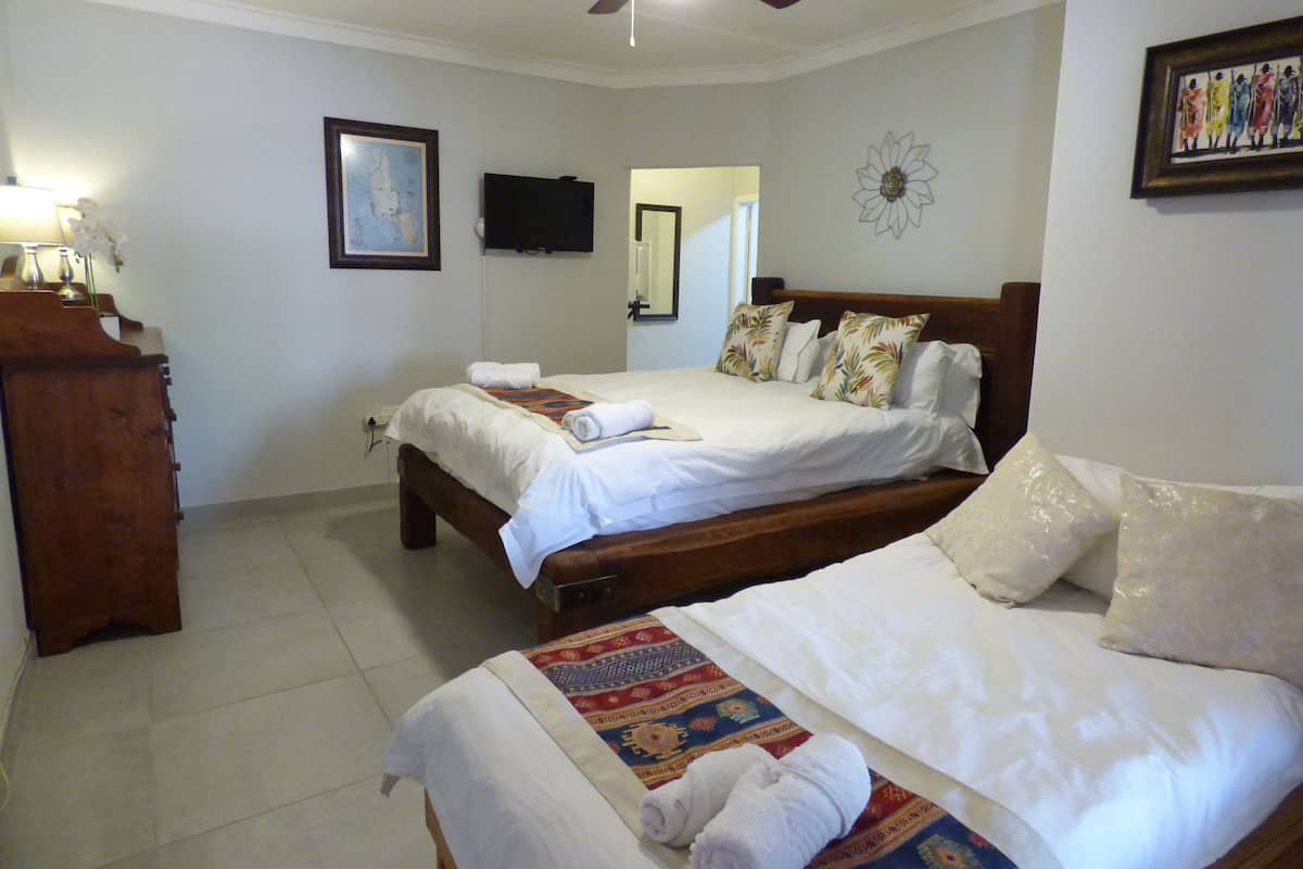 A hotel room with two beds, a wooden dresser, a ceiling fan, a framed map, and a wall-mounted TV.