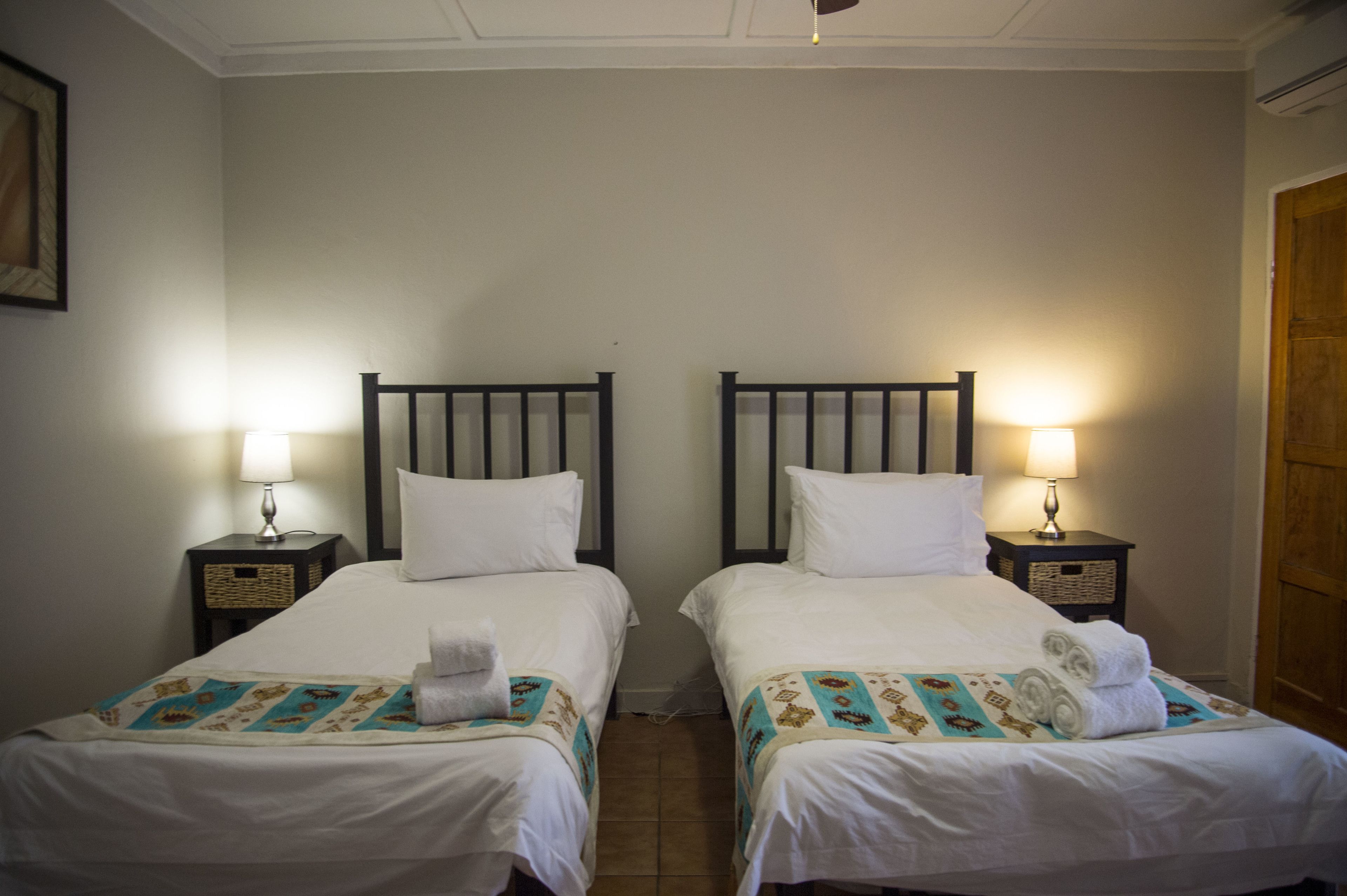 Ein Hotelzimmer mit zwei Einzelbetten, jeweils mit Kopfteil, Nachttischen und Lampen.