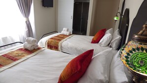 A hotel room with two beds, each with white linens and red pillows. There are towels stacked on the beds, and a decorative lamp is visible. - Tsumeb Backpackers & Safari (Tsumeb)