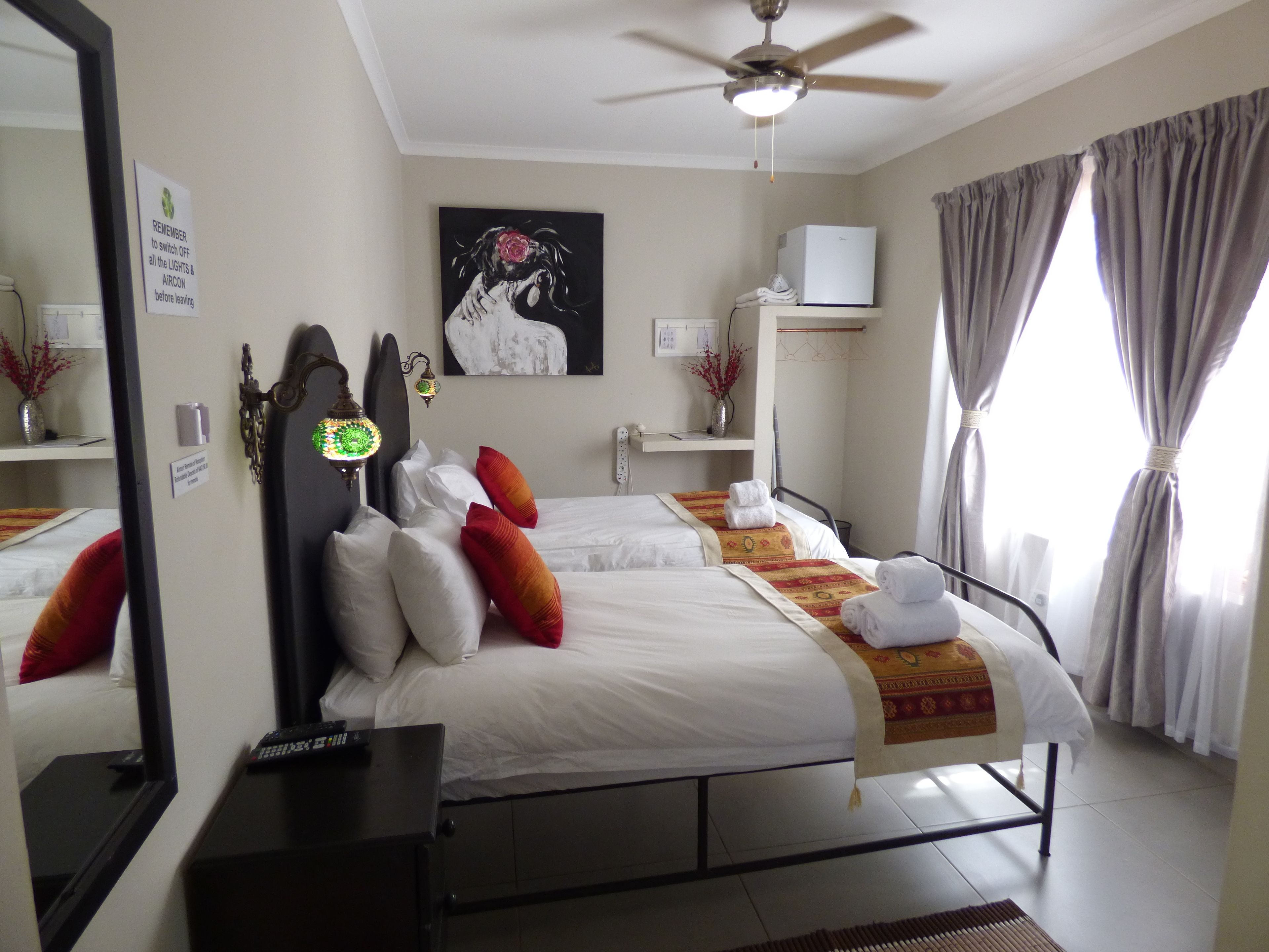 A hotel room with a bed, bedside tables, a ceiling fan, a painting, and a window with curtains.