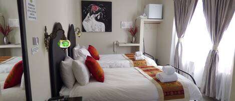 A hotel room with a bed, bedside tables, a ceiling fan, a painting, and a window with curtains.