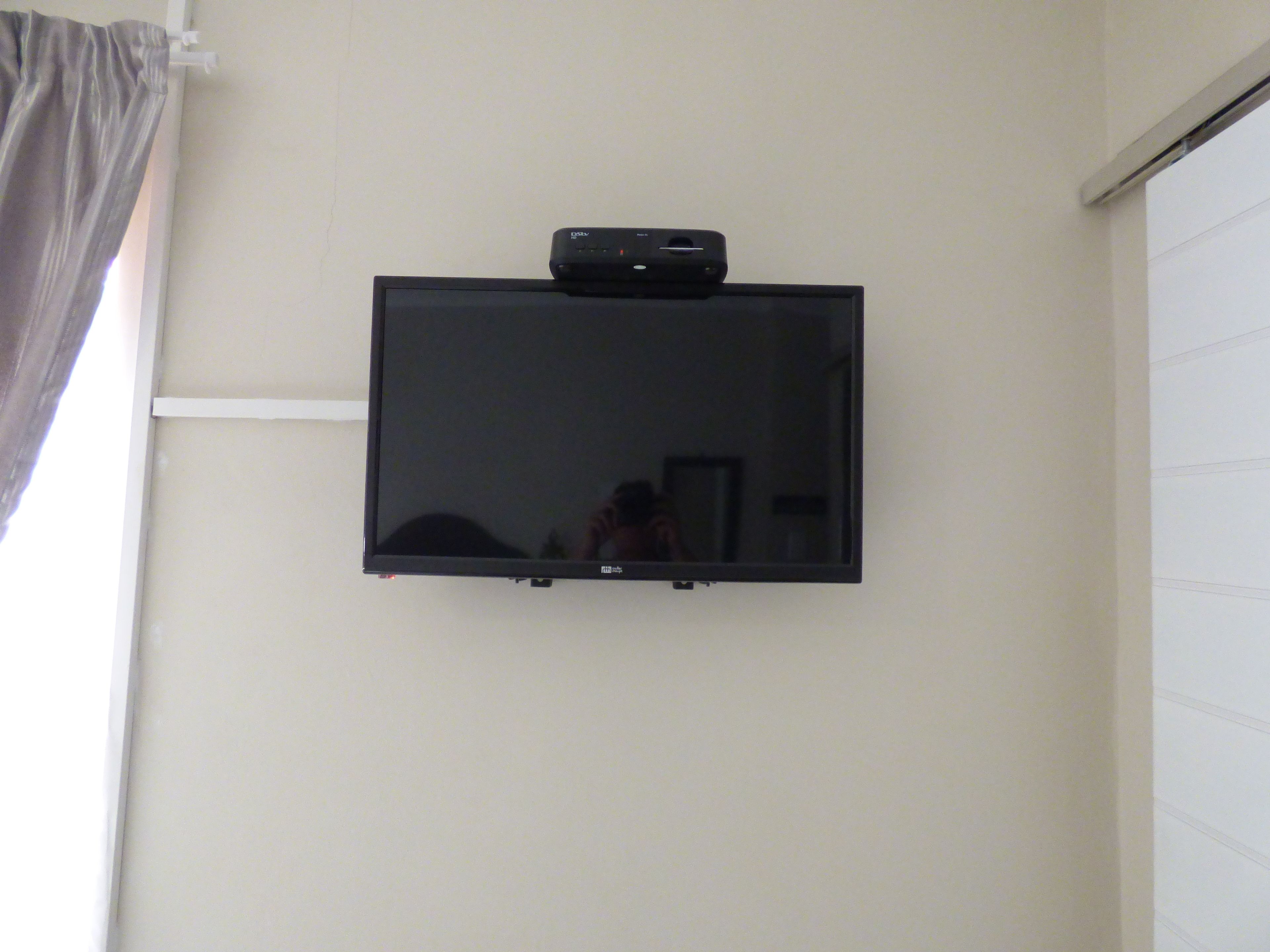 A flat-screen TV mounted on a wall with a cable box above it.