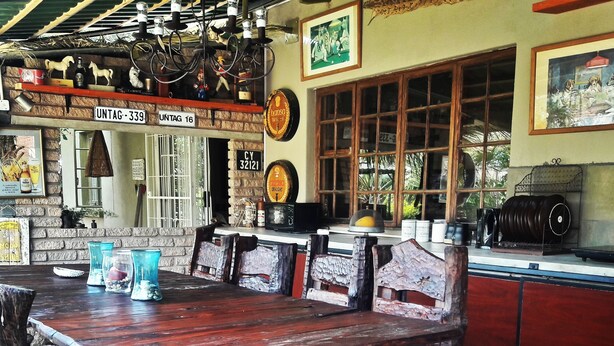 A rustic wooden table with benches, a brick wall, and a window with a view of greenery. - Tsumeb Backpackers & Safari (Tsumeb)