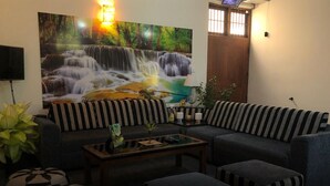 Een woonkamer met een hoekbank, gestreepte poefjes, een salontafel en een groot schilderij van een waterval.