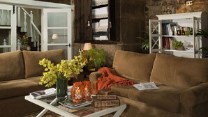 A cozy living room with a wooden ceiling, a stone wall, a brown sofa, a white coffee table, and a bookshelf. - A Casa da Torre Branca (Santiago de Compostela)