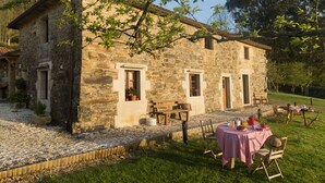 A stone building with a patio area, outdoor seating, and a table set for a meal. - A Casa da Torre Branca (Santiago de Compostela)