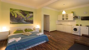 A bedroom with a bed, bedside lamps, and a green pillow. There is a bathroom with a sink and a mirror. The room has wooden flooring and a green wall. - Apartment for Friends (Prague)