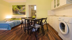 A compact living space with a bed, a dining table with chairs, a washing machine, and a kitchen area with cabinets. - Apartment for Friends (Prague)