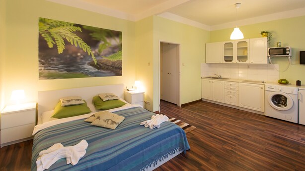 A bedroom with a bed, green pillows, a blue striped bedspread, and a large fern wall art. - Apartment for Friends (Prague)