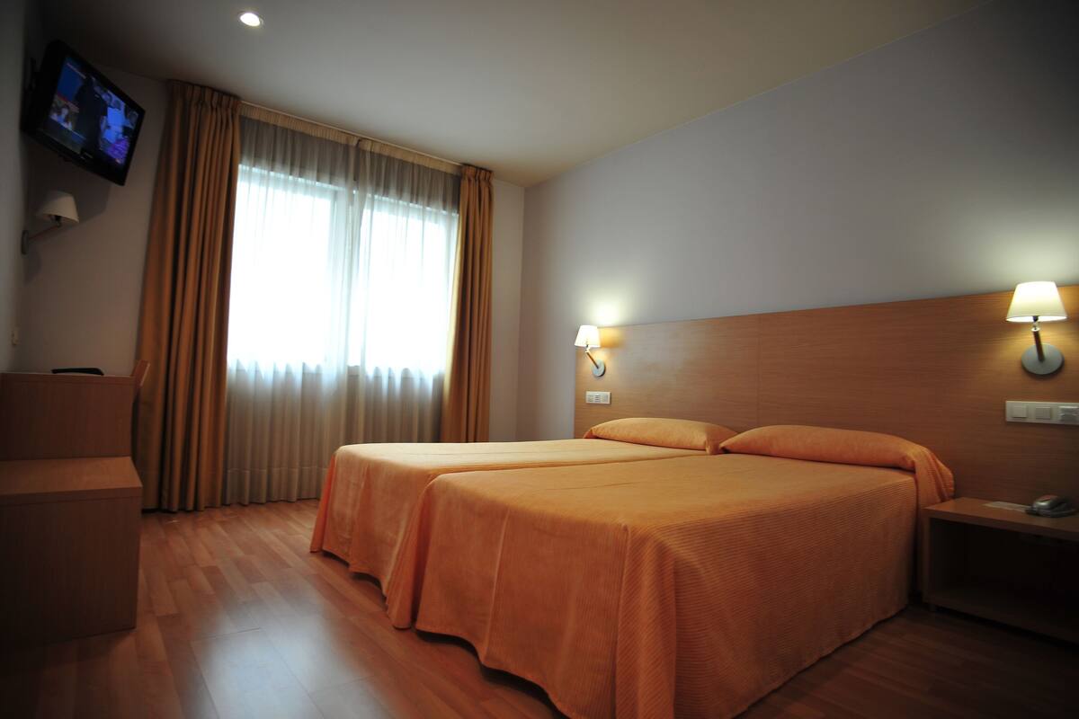 Quarto de hotel com duas camas, televisão e escrivaninha.