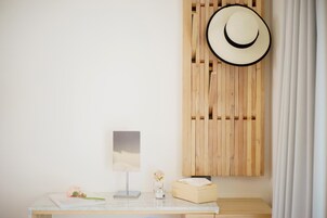 A minimalist room with a wooden slat wall, a white desk with a lamp, a vase with flowers, and a hat hanging on the wall.