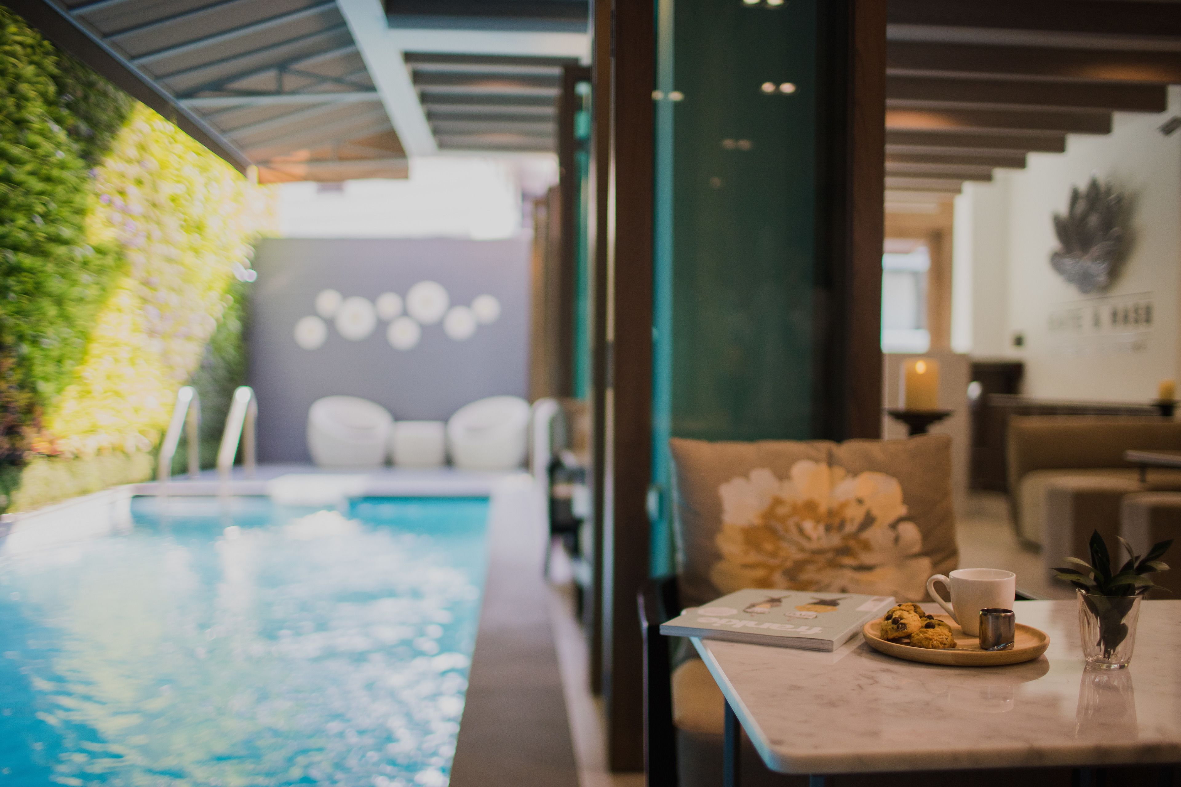 A modern indoor pool area with a glass table, a coffee cup, and a plate of cookies.