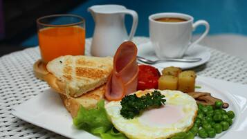 Un plato de comida para el desayuno con tostadas, jamón, huevo, guisantes y papas, junto a un vaso de jugo de naranja y una taza de café.