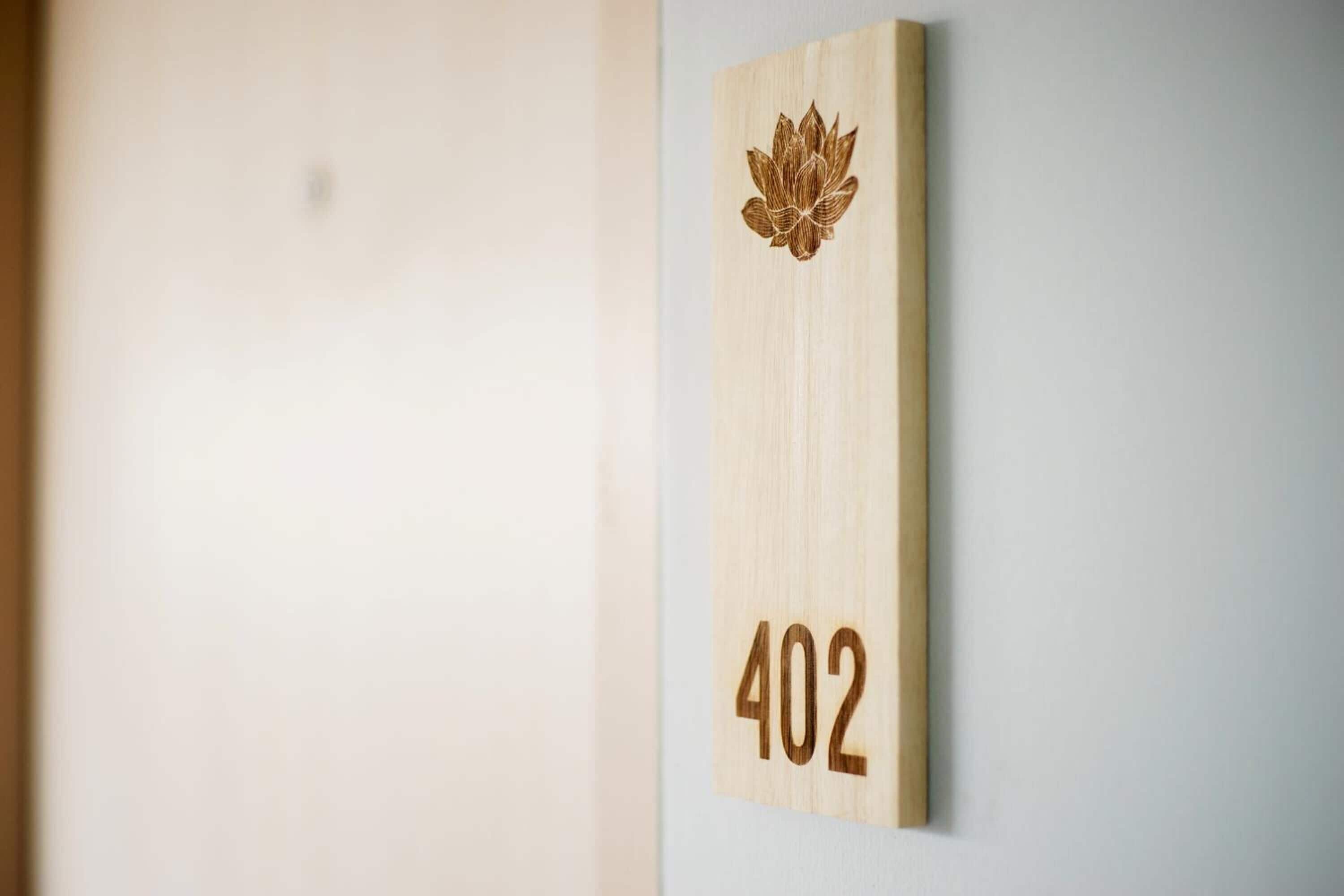 A wooden wall-mounted sign with a lotus flower and the number 402.