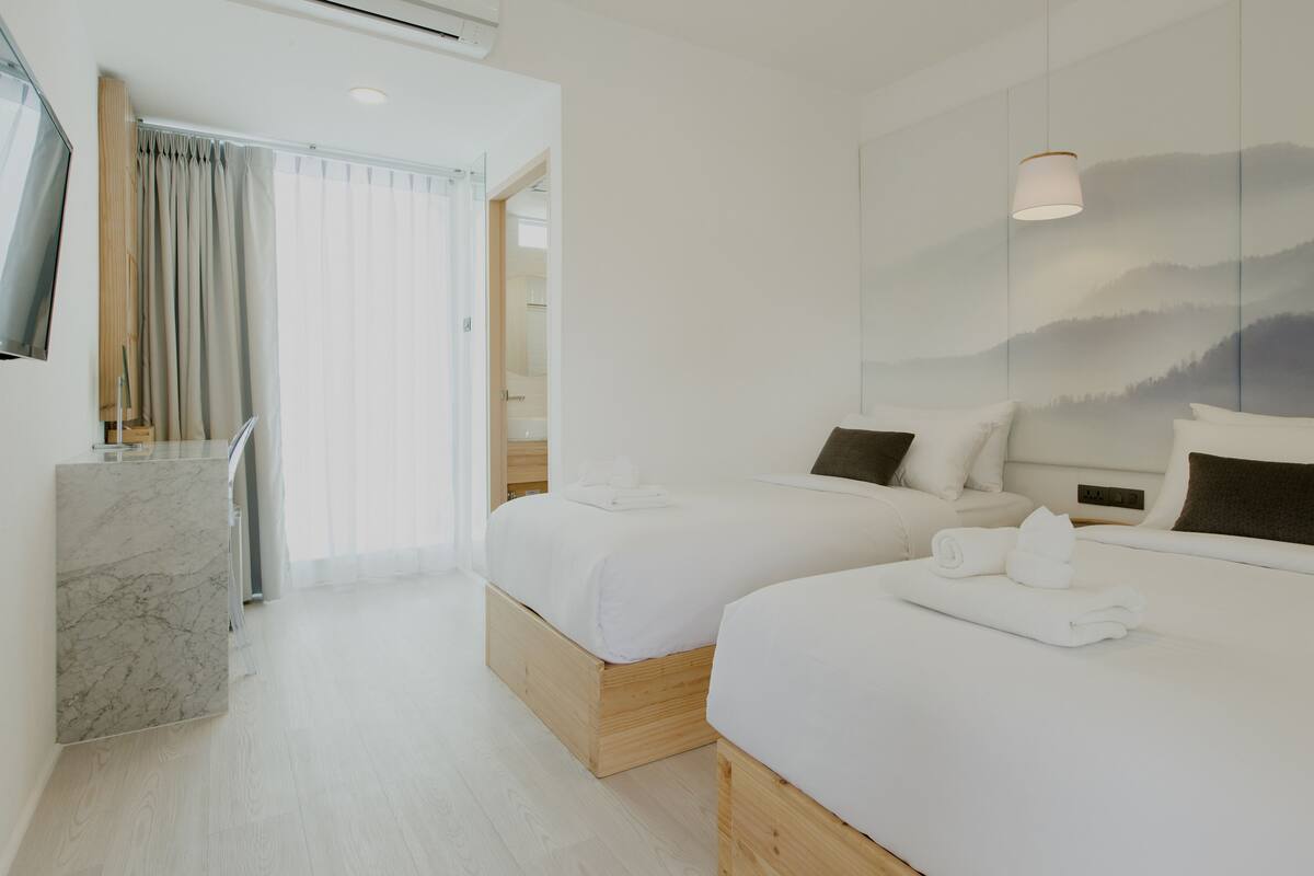 Habitación de hotel con dos camas, un escritorio de madera, un televisor de pantalla plana y un gran ventanal con cortinas.