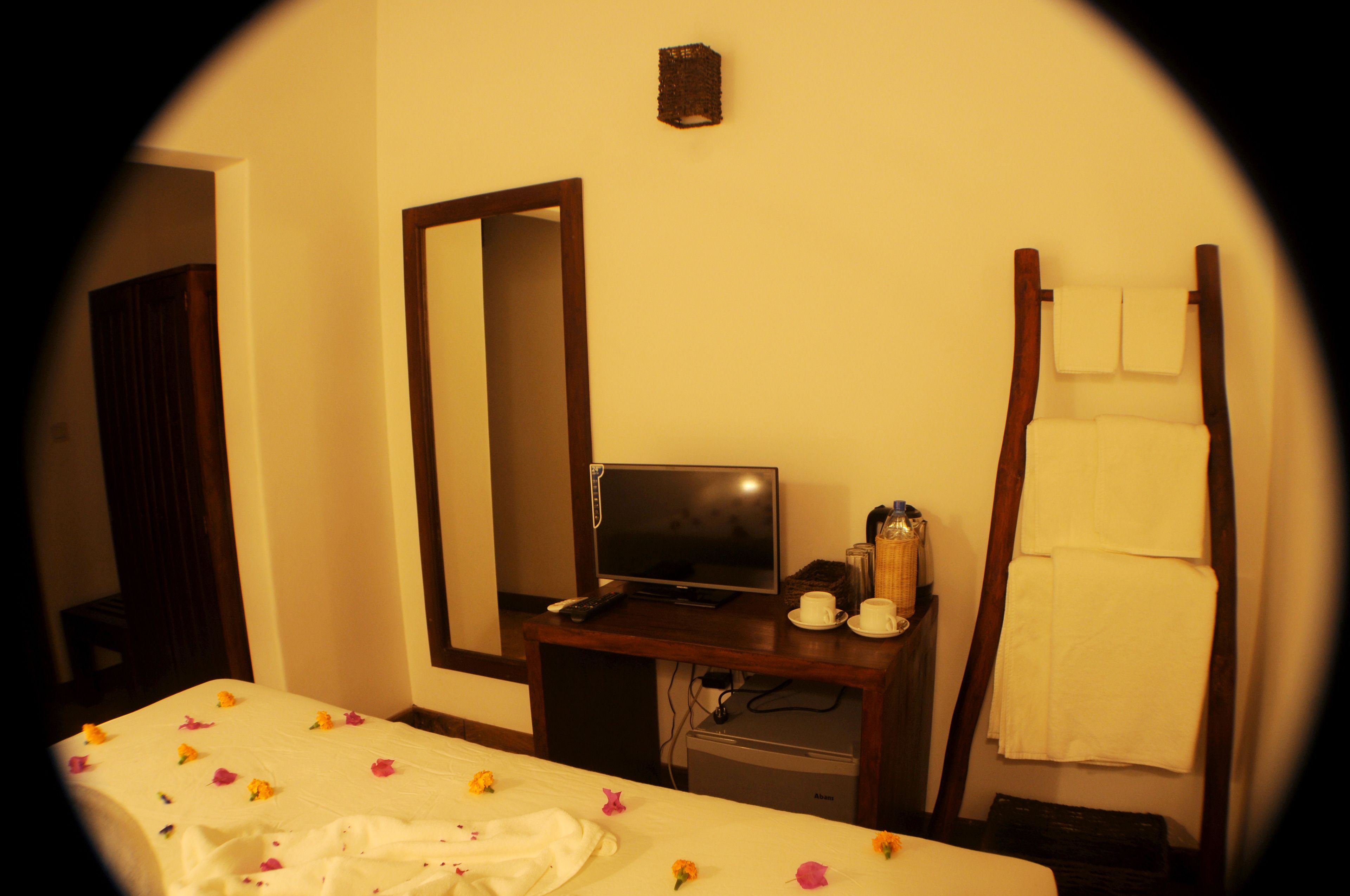 A hotel room with a bed, a desk with a television, a mirror, and a towel rack.