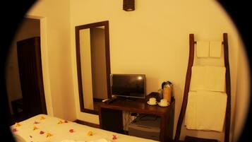 A hotel room with a bed, a desk with a television, a mirror, and a towel rack.