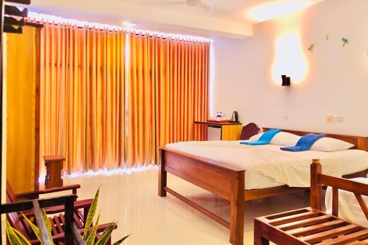 A hotel room with a wooden bed, a bedside table, a nightstand, a chair, and a potted plant.