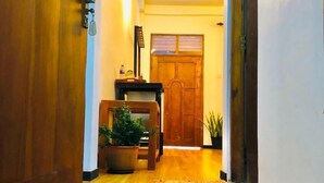 Un pasillo con suelo de madera, una planta en maceta, una mesita con lámpara y una puerta al final.