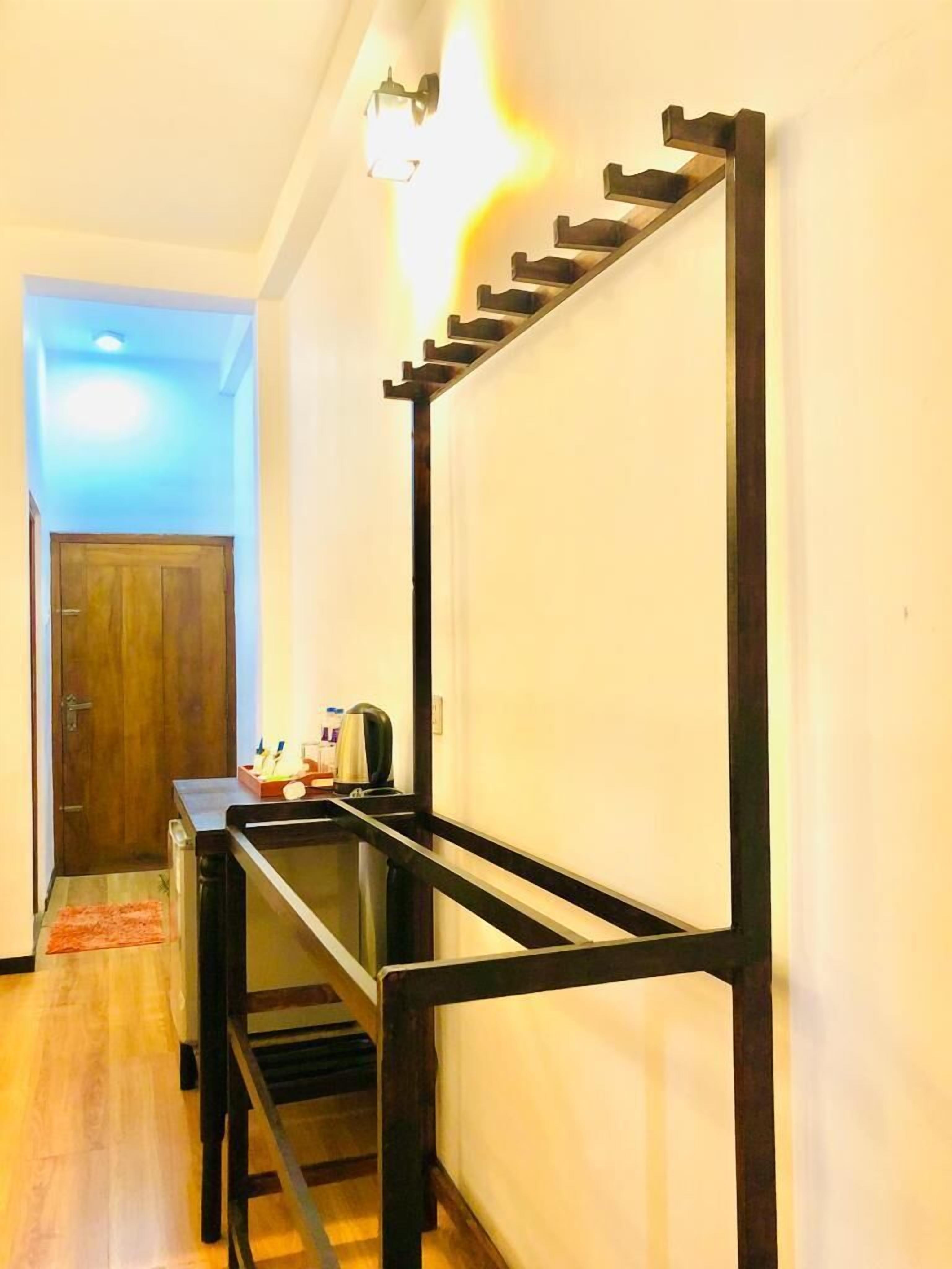 A hallway with a wooden door, a small table with a kettle, and a black metal rack against the wall.