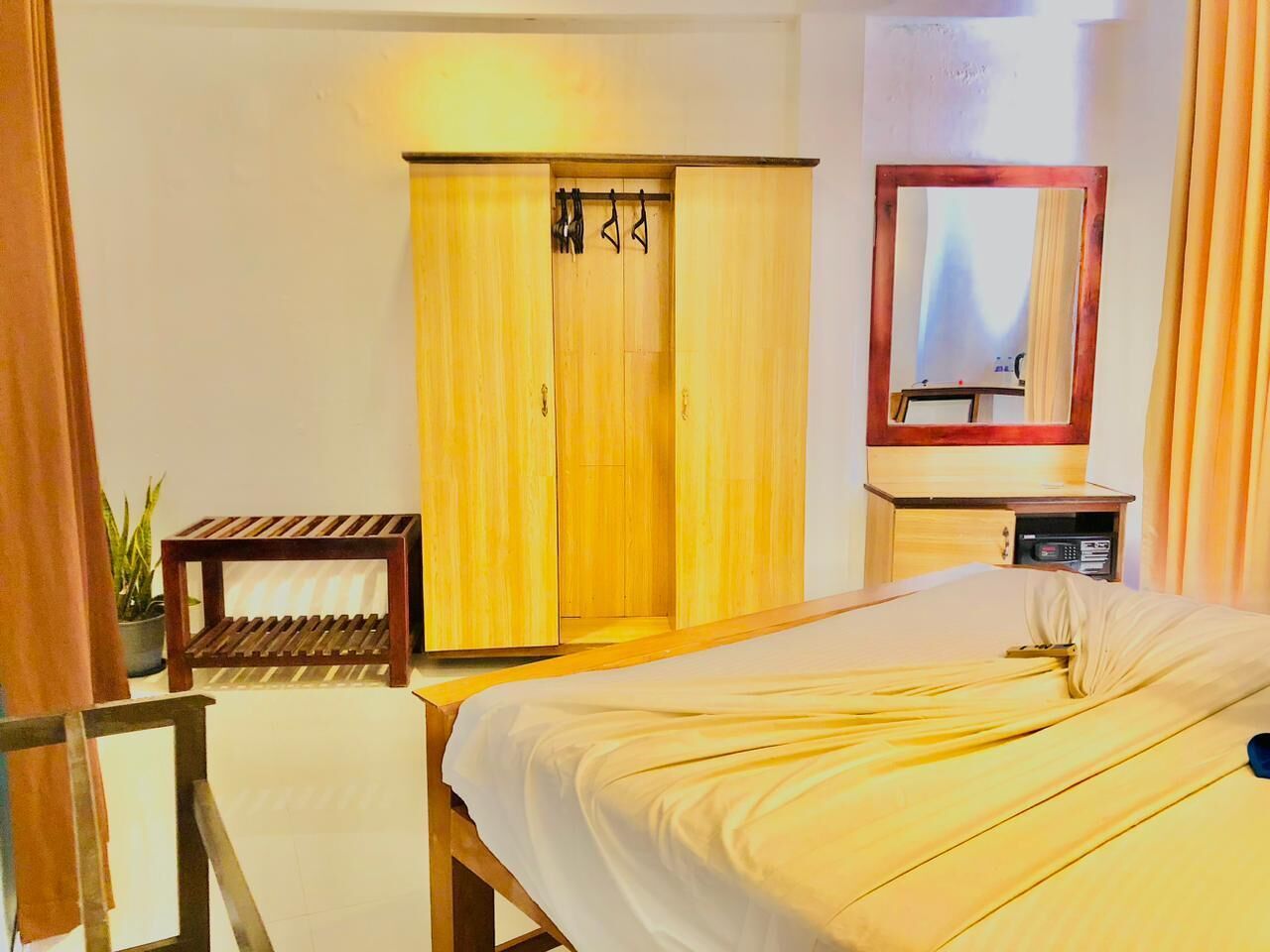 Una habitación de hotel con cama, armario de madera, una mesita y un espejo.