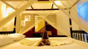 Una habitación con cama bajo dosel, cabecera de madera, mesita de noche y cartel en la pared.