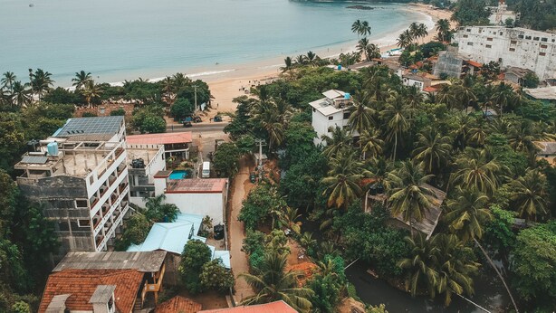 Un pueblo costero con playa, densas palmeras y un faro.