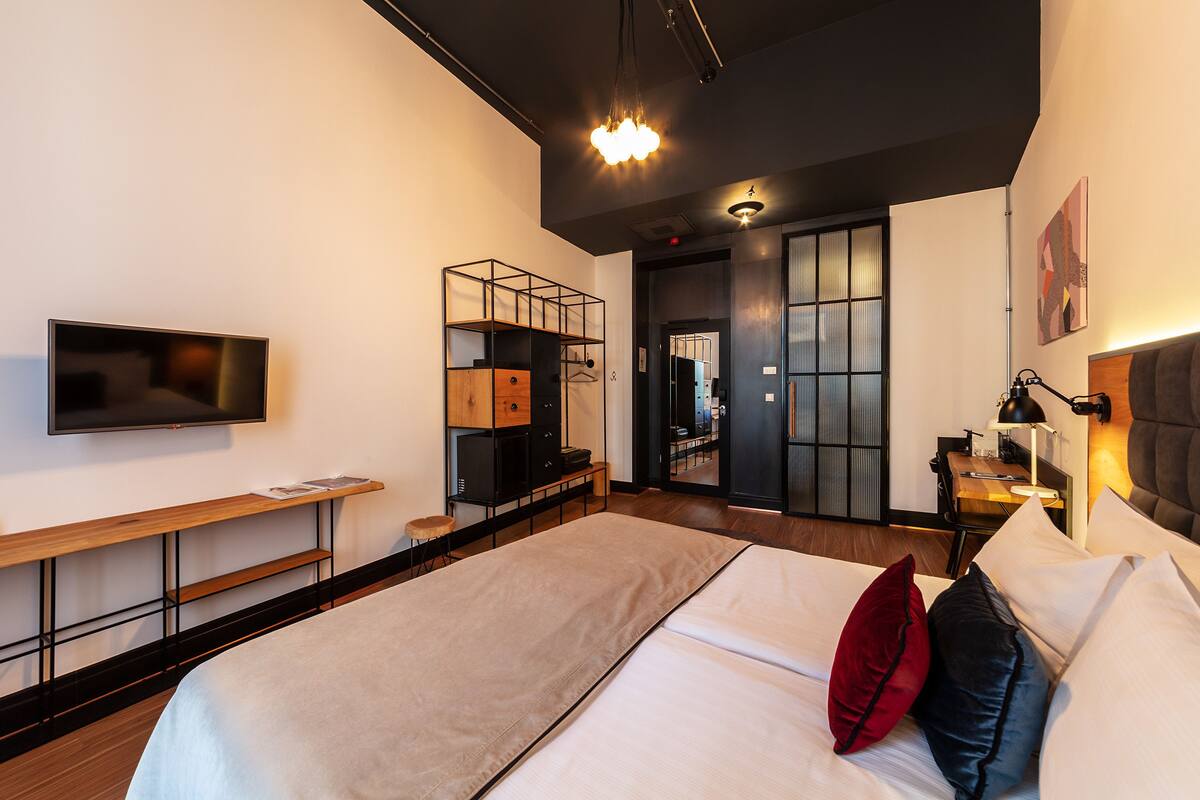 A modern hotel room with a large bed, a flat-screen TV, a desk with a lamp, and a walk-in closet.