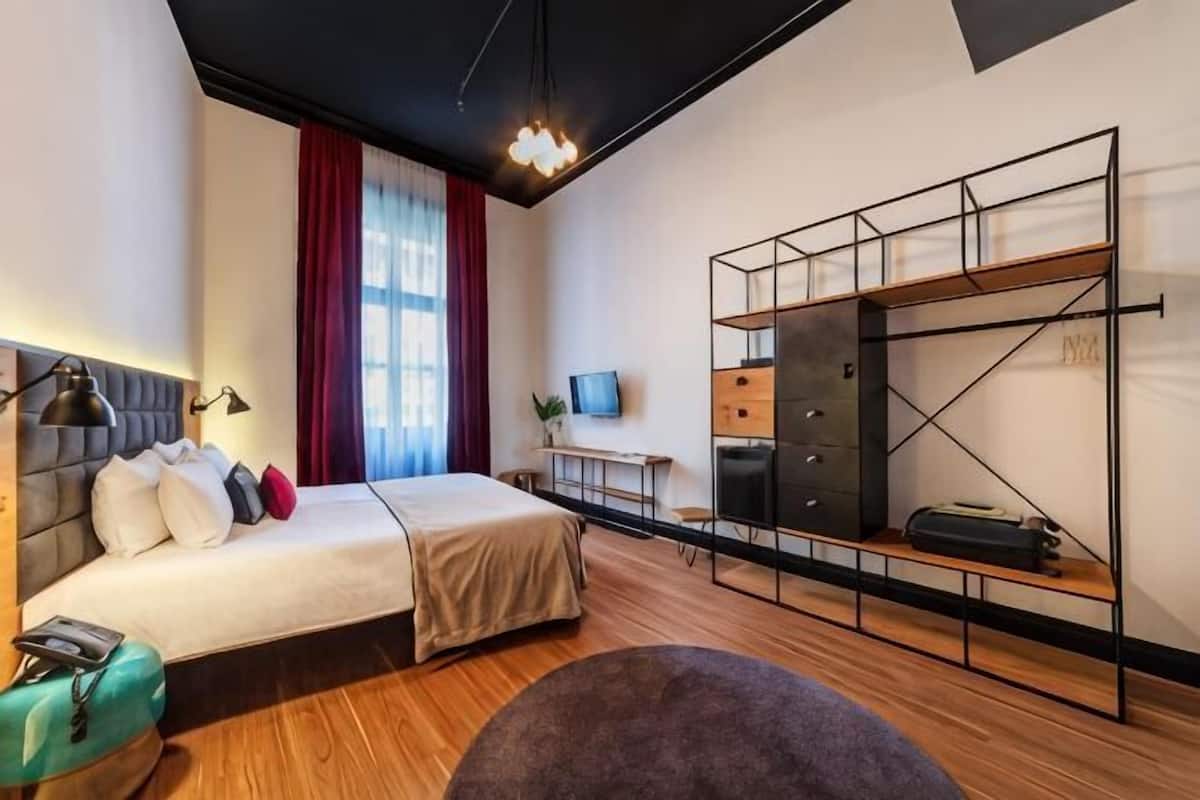 A modern hotel room with a bed, a desk, a TV, and a built-in wardrobe.