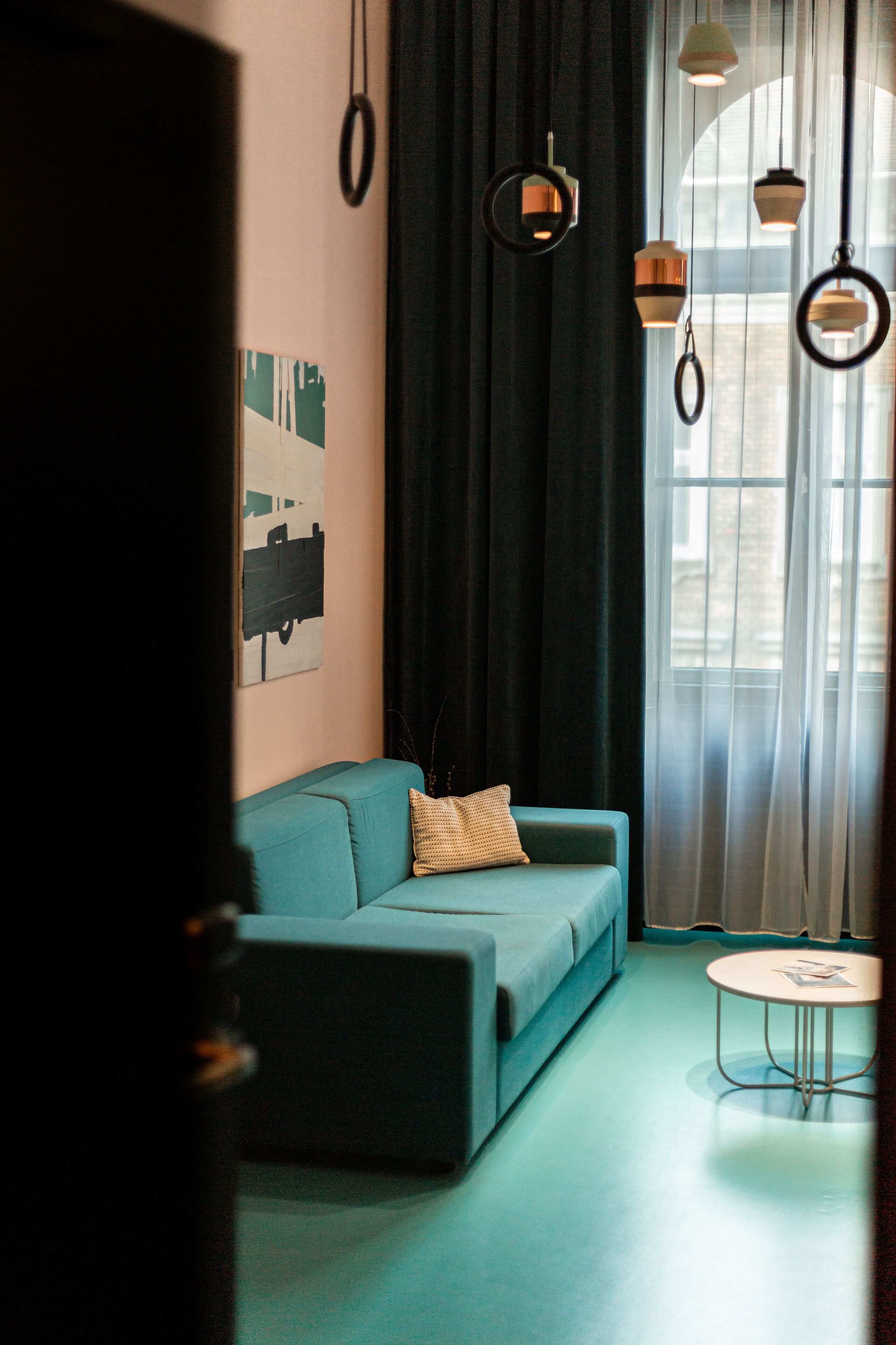 Una sala moderna con un sofá color turquesa, una mesita redonda y lámparas colgantes.