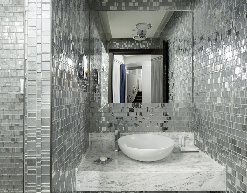 A bathroom with a large, round sink, tiled walls, and a mirror.