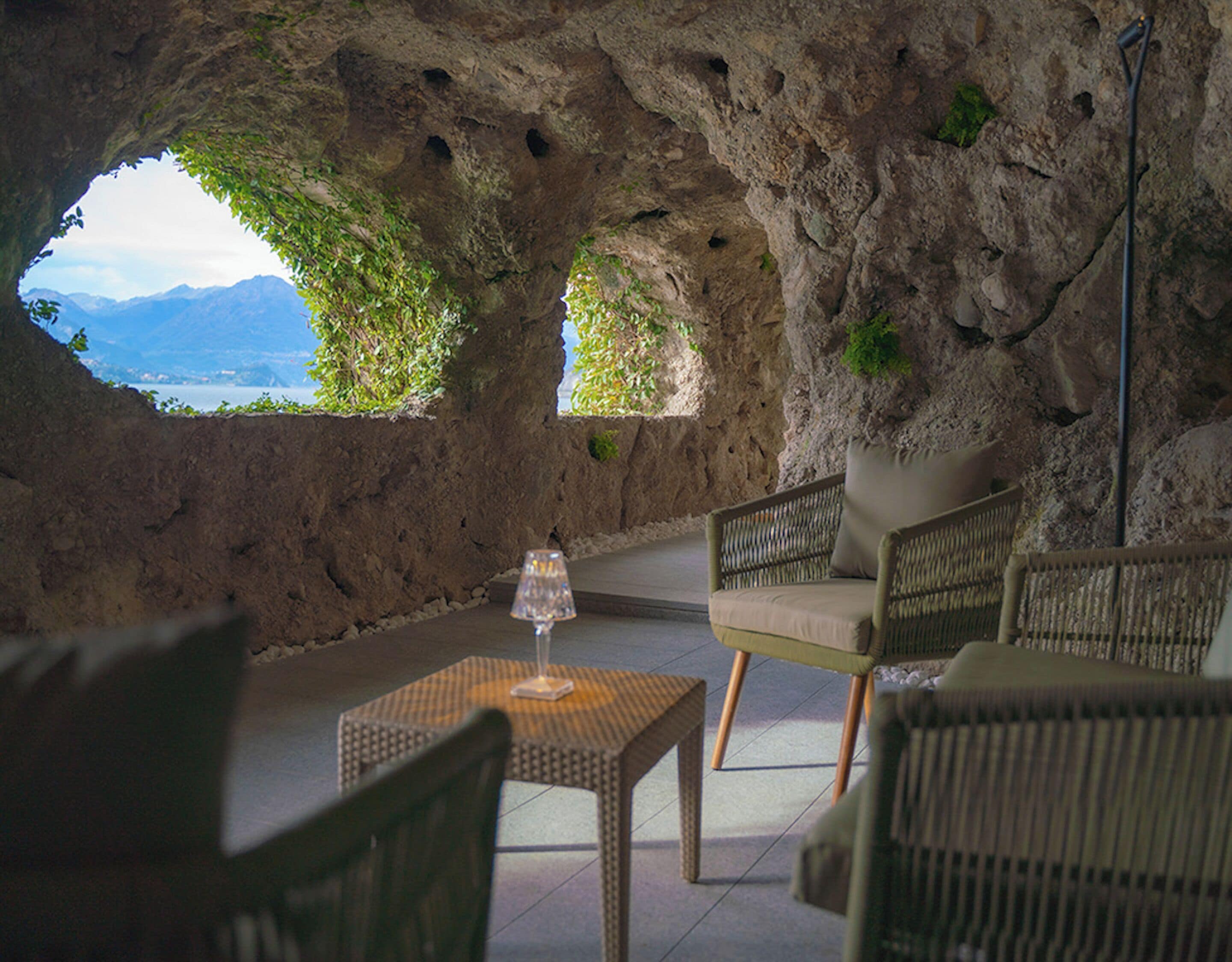Ein hohlenartigen Innenraum mit Korbmöbeln und einem Glastisch, mit Blick auf eine Berglandschaft.