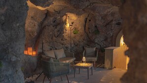 A cozy outdoor seating area with wicker chairs and a small table, set against a rocky backdrop with ambient lighting.