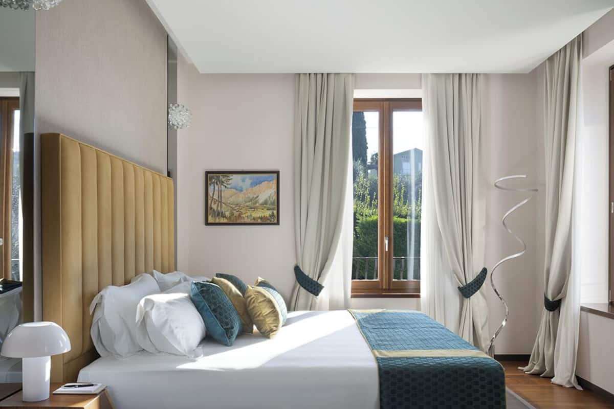A modern hotel room with a large bed, a bedside table, a lamp, and a window with curtains.