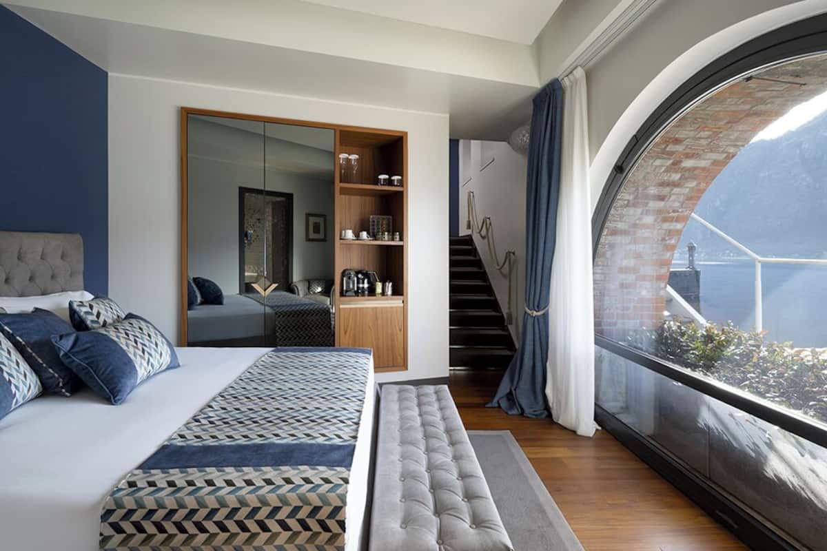 A modern bedroom with a large bed, a built-in wardrobe, a seating area, and a large window with a view of the outdoors.