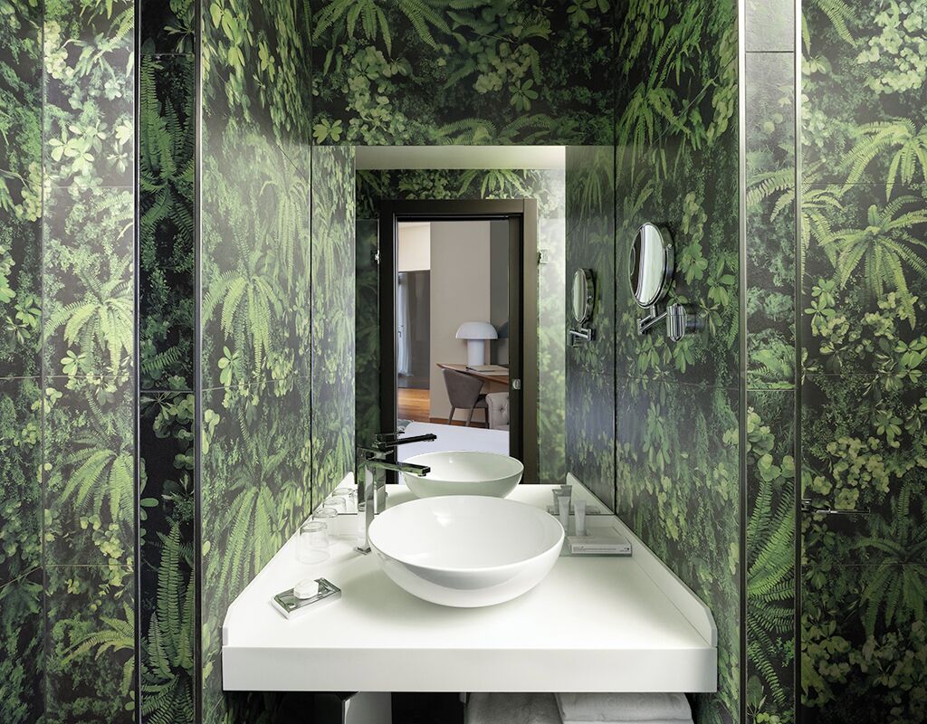 Une salle de bain avec un lavabo blanc, deux miroirs et une porte donnant sur une pièce.