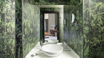 Une salle de bain avec un lavabo blanc, deux miroirs et une porte donnant sur une pièce.