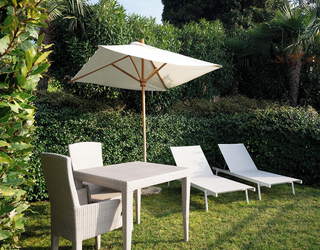 Un patio con una mesa, dos sillones, una sombrilla y abundante vegetación de fondo.