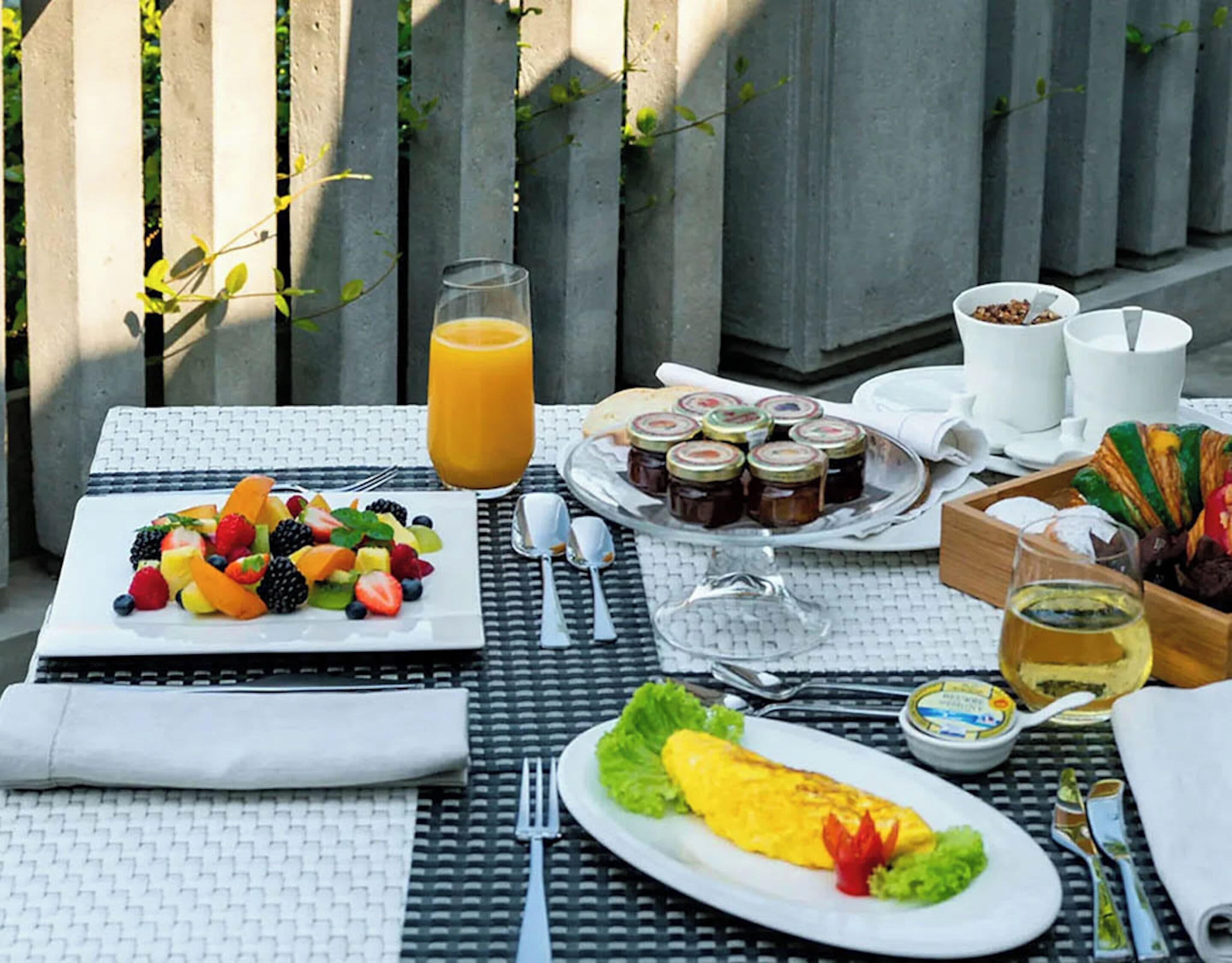 Ett bord dukat med frukosttillbehör, inklusive frukt, sylt och en omelett, samt ett glas apelsinjuice.