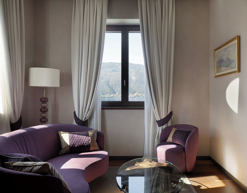 Un soggiorno moderno con un divano viola, un tavolino da caffè in vetro e vista su un paesaggio montuoso attraverso una grande finestra.