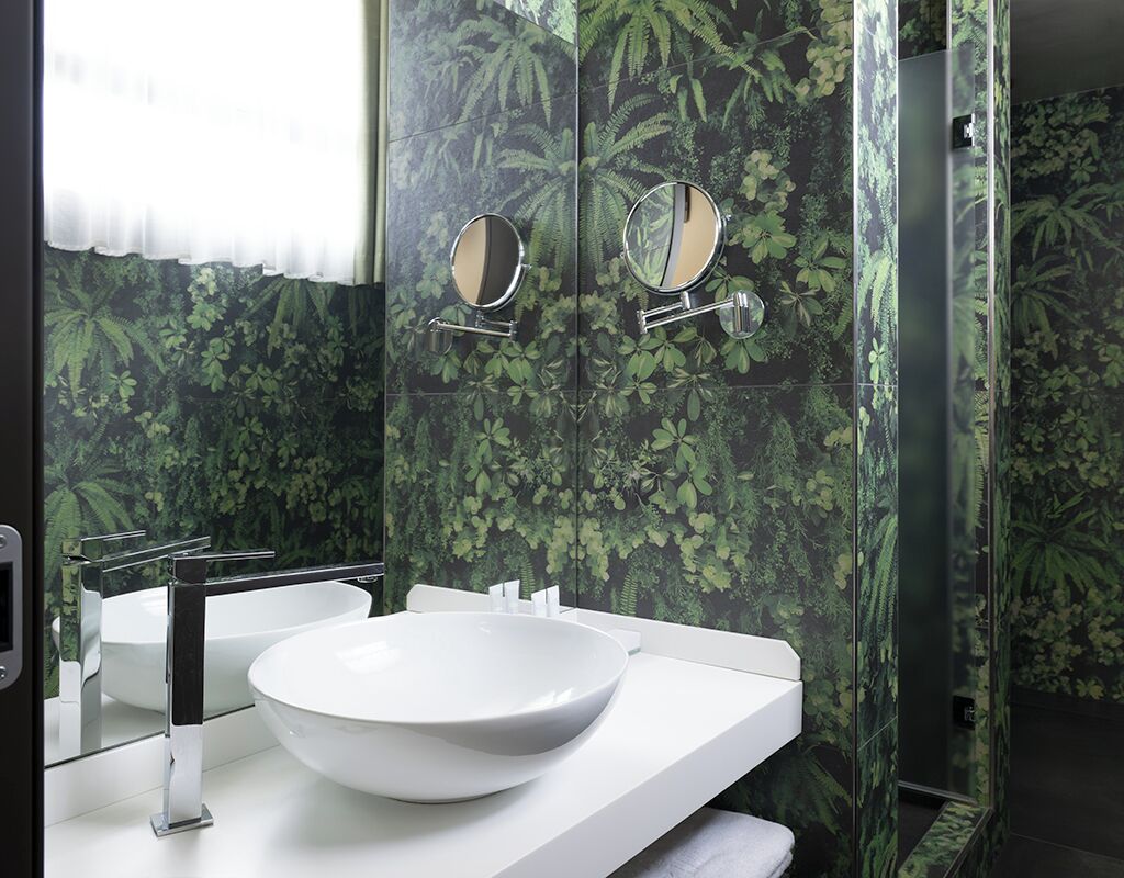 A bathroom with a white sink, two mirrors, and a green leaf-patterned wall.