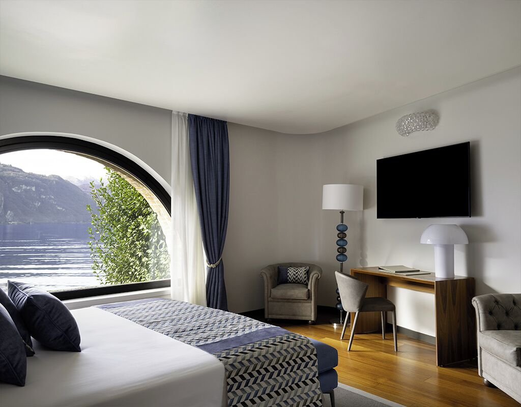 Ett hotellrum med en säng, två stolar, ett skrivbord, en tv och utsikt över en sjö eller ett annat vattendrag.