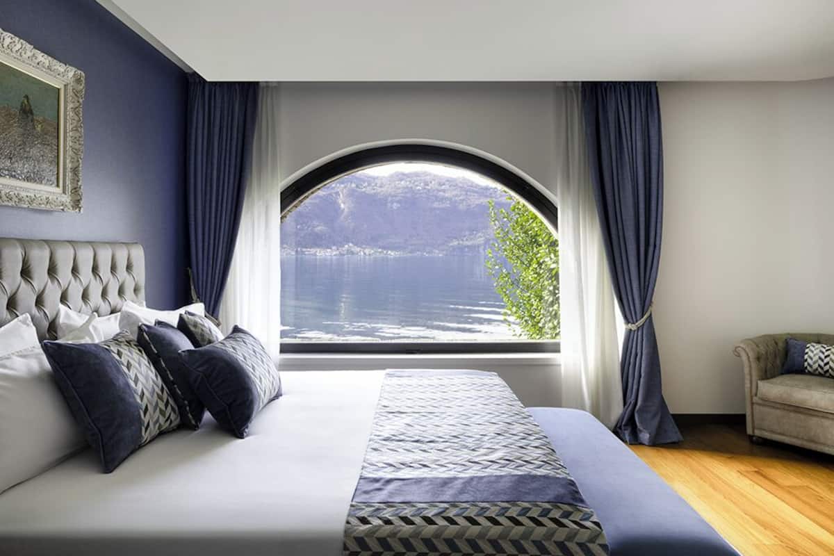 A bedroom with a large bed, a view of a lake, and a window with curtains.