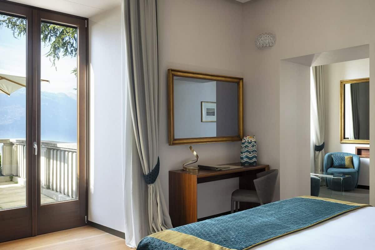 A hotel room with a bed, a desk, a chair, a large mirror, and a view of the outdoors.