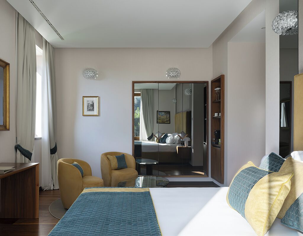 Una moderna camera d'albergo con un letto grande, una zona salotto con una poltrona, una scrivania e uno specchio.