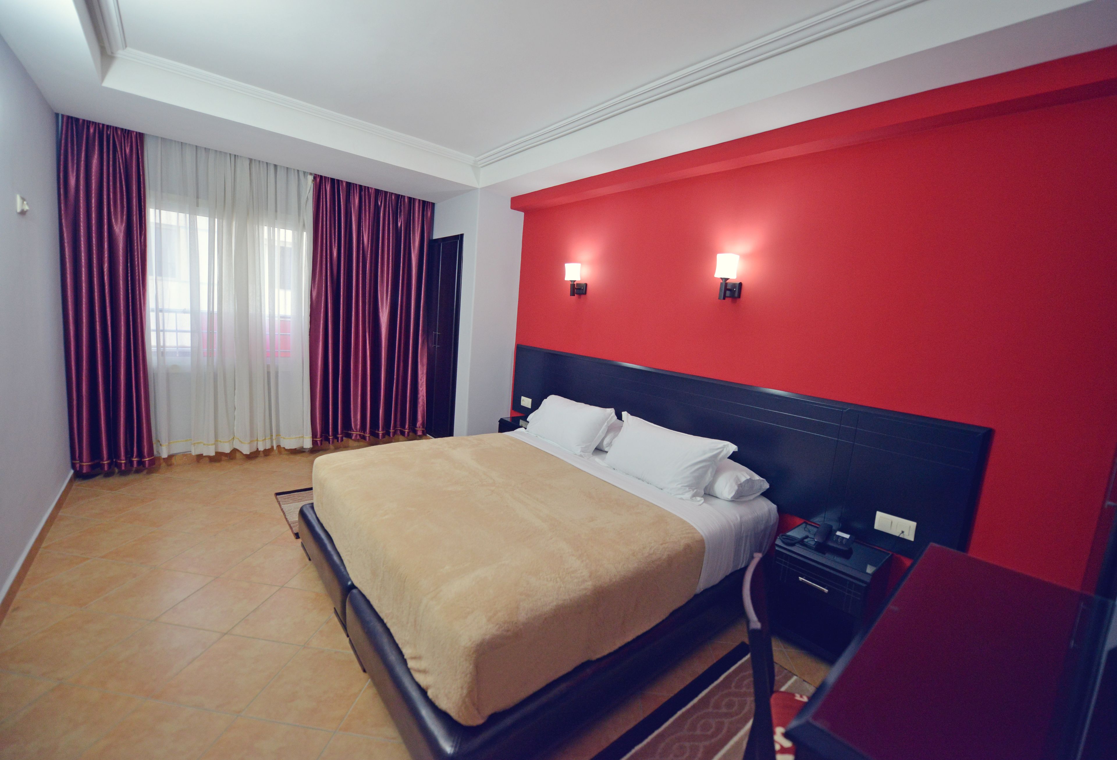 Una habitación de hotel con una cama grande, paredes de acento rojas y una mesita de noche con lámpara.