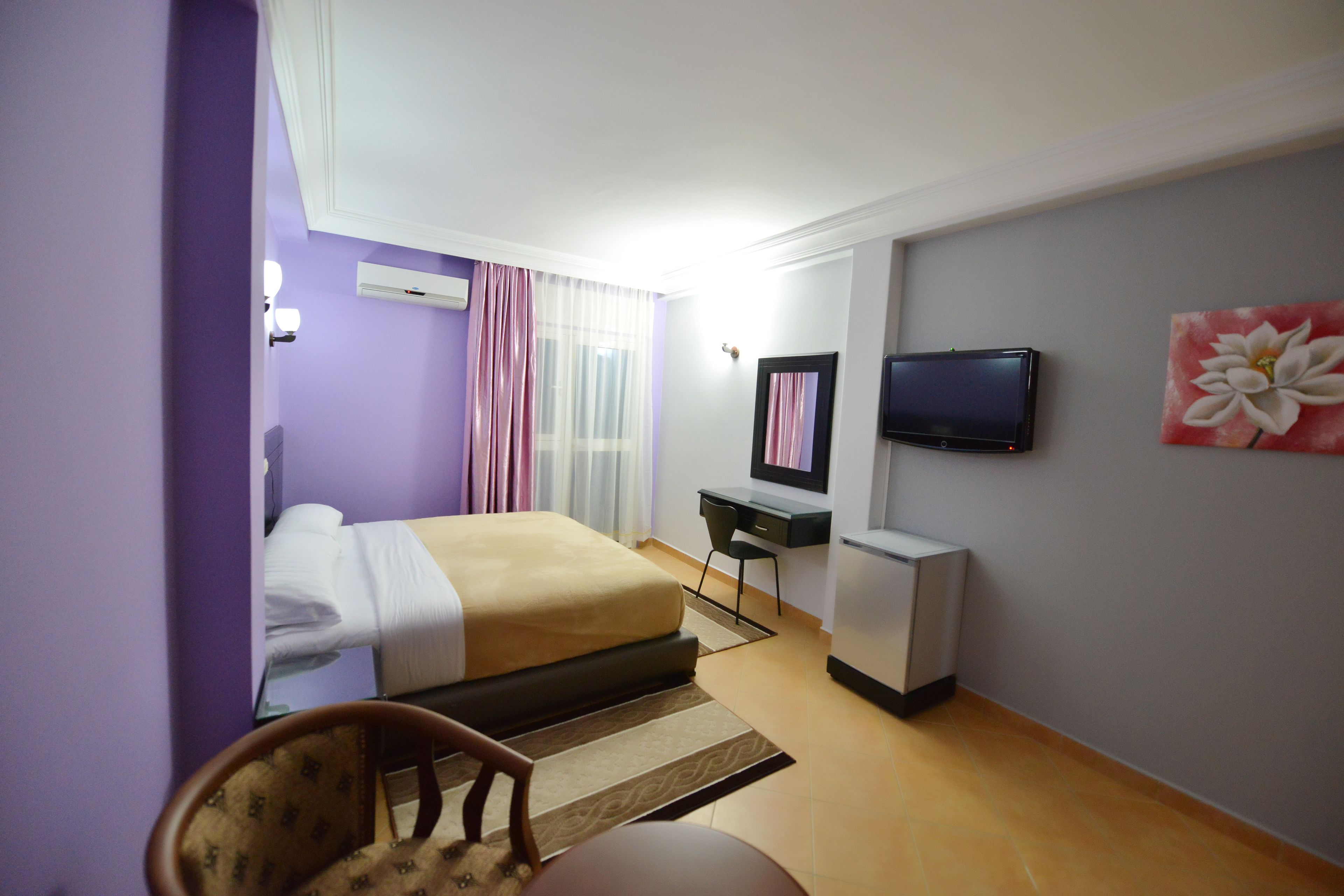 Una habitación de hotel con cama, escritorio, silla, televisor y una obra de arte en la pared.