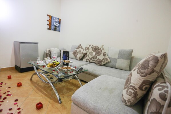 A living room with a sofa, a glass coffee table, and a small refrigerator. - Hôtel Suite Martil (Martil)