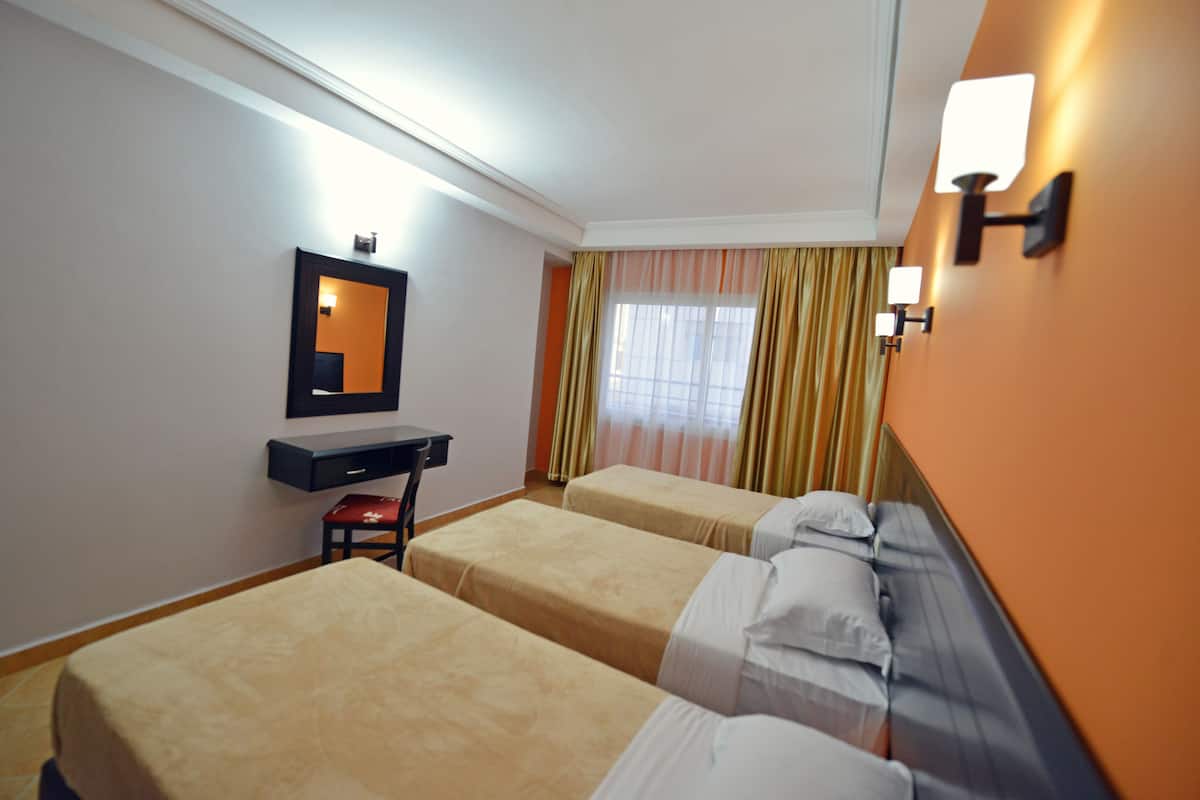 A hotel room with two single beds, a desk, a chair, a mirror, and a window with curtains.