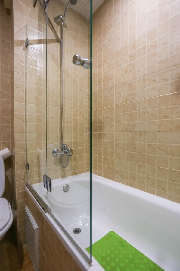 Un baño con ducha de vidrio, una bañera blanca y paredes de cerámica color beige.